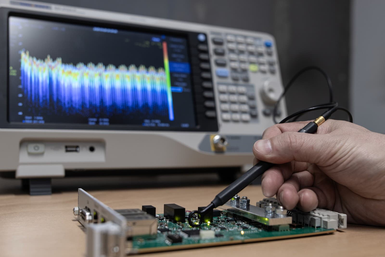 Near-field probe above a circuit board, with a spectrum analyzer in the background